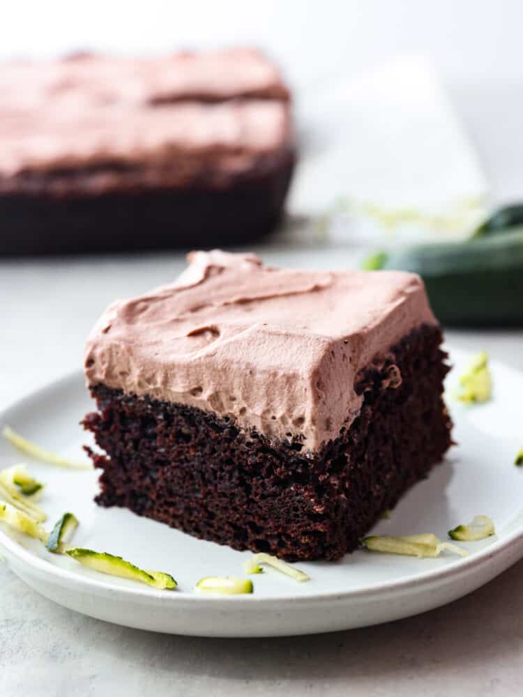 This Chocolate Zucchini Cake is a deep, dark chocolate cake that is topped with light and fluffy chocolate whipped cream! With 3 cups of zucchini, it is incredibly moist and you won't even notice all the vegetables! A slice of chocolate zucchini cake on a plate.