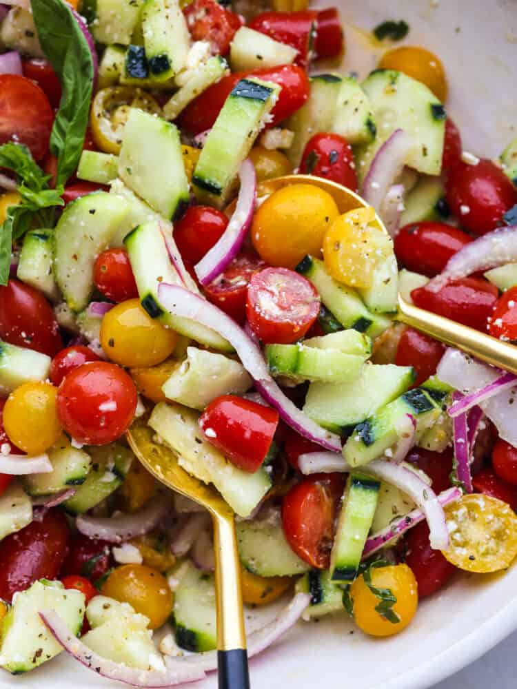 Chilled Cucumber Tomato Salad is a refreshing salad made with fresh ingredients that everyone can enjoy all year round. It's fast, easy, and can be made ahead, making it perfect for any potluck! A close up of cucumber tomato salad in a bowl with a gold spoon.