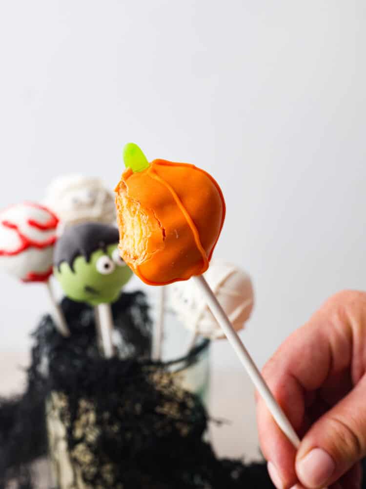These easy, festive, and adorable Halloween donut hole pops will thrill your guests! Believe me when I say people can't stop talking about how adorable, and how delicious these pops are. You'll be so glad you served these at your Halloween party this year. A pumpkin-shaped donut hole pop with a bite taken out of it.