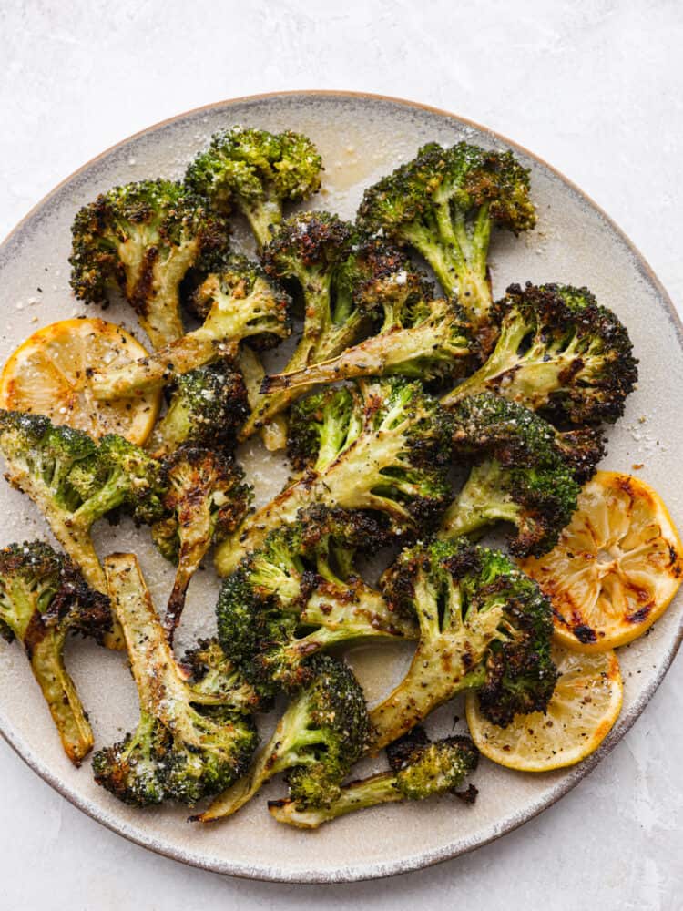 The perfect side dish for summer, parmesan garlic grilled broccoli is cooked to perfection and packed with so much flavor! It's the best addition to any barbecue. Top-down view of grilled broccoli on a stoneware plate.