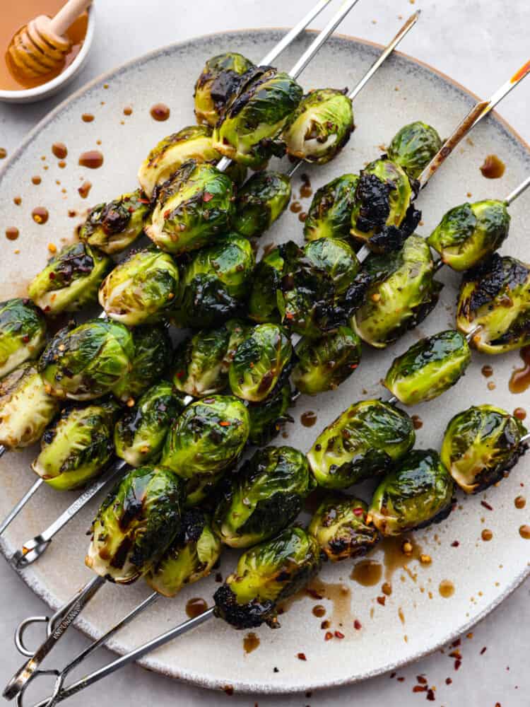 Crispy on the outside, tender on the inside, and topped with a balsamic honey glaze, these grilled brussels sprouts are the best side dish for summer and early fall! The amazing tangy flavor and tender, caramelized texture of these brussels sprouts will make even the pickiest of eaters a fan. Top-down view of grilled brussels sprouts on a gray stoneware plate.