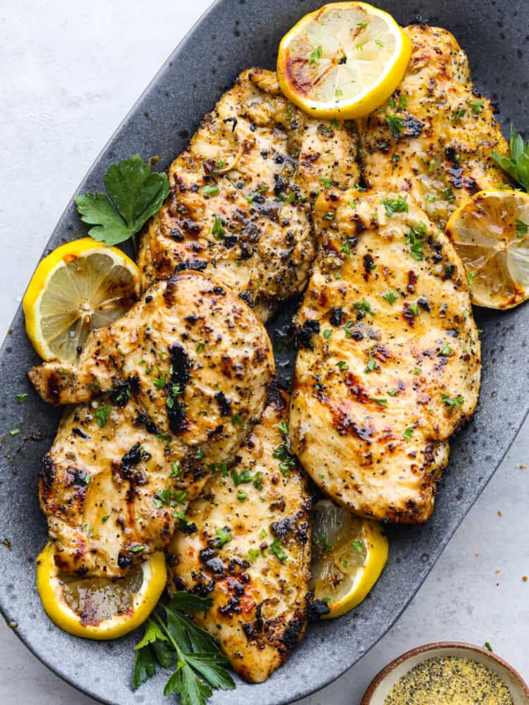 This grilled lemon pepper chicken is the perfect summer grilling recipe! This juicy chicken is packed with lemon, garlic and onion flavors that will make your mouth water and keep you coming back for more! The top view of grilled lemon pepper chicken on a gray platter.