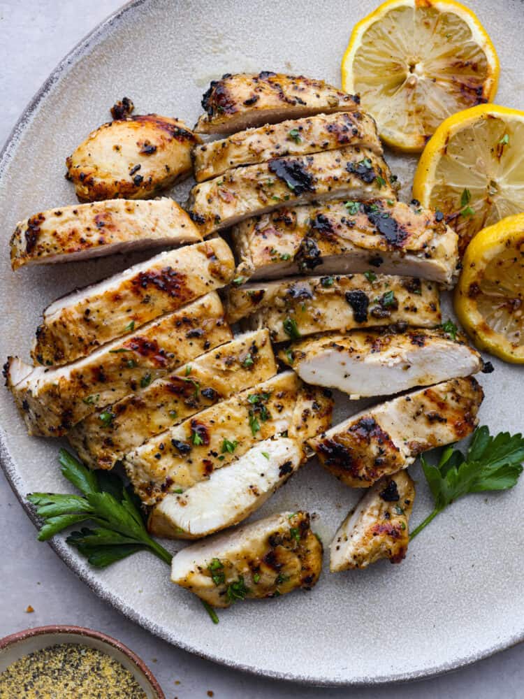 This grilled lemon pepper chicken is the perfect summer grilling recipe! This juicy chicken is packed with lemon, garlic and onion flavors that will make your mouth water and keep you coming back for more! Grilled chicken on a plate, sliced and ready to eat.
