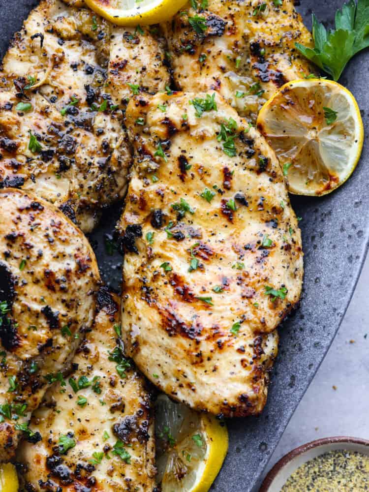This grilled lemon pepper chicken is the perfect summer grilling recipe! This juicy chicken is packed with lemon, garlic and onion flavors that will make your mouth water and keep you coming back for more! Grilled lemon pepper chicken on a platter with lemon slices.