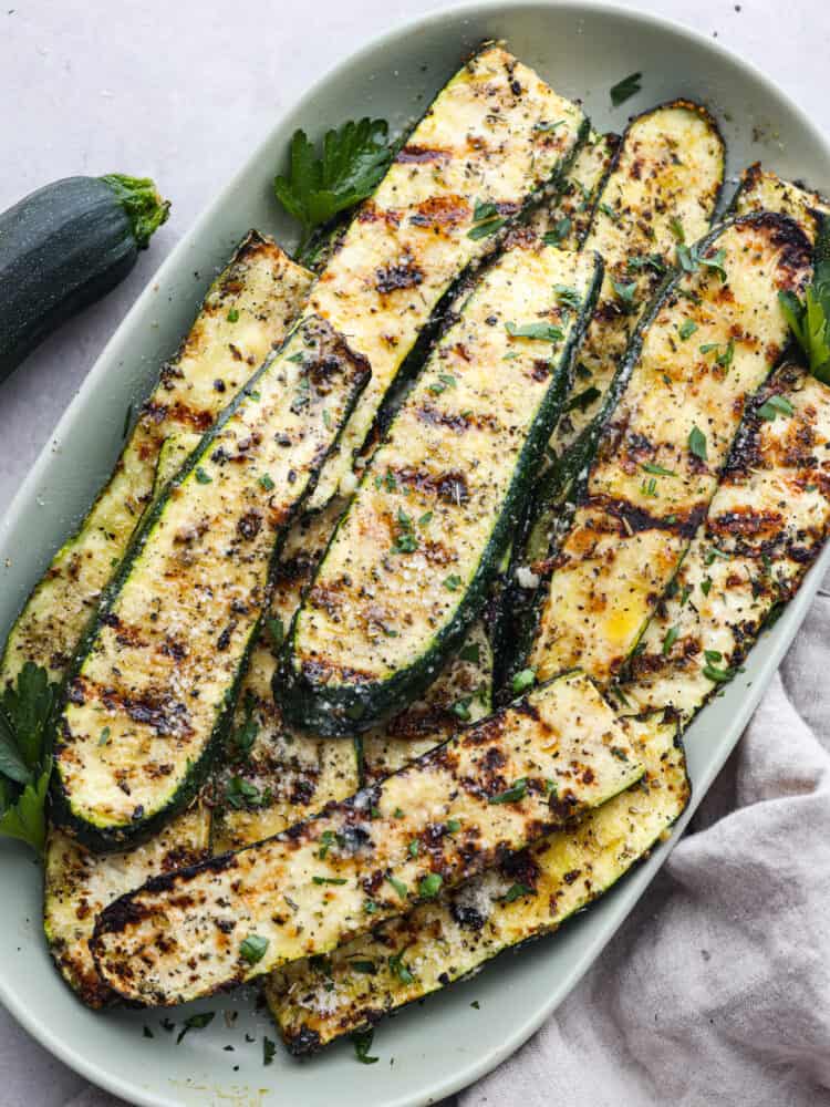 If you're not making zucchini bread with all of that home-grown zucchini, then you HAVE to try this grilled zucchini! Light, smoky, and perfectly seasoned, it cooks up in minutes and goes with just about everything. Slice, grilled zucchini seasoned and ready to eat in a white bowl.