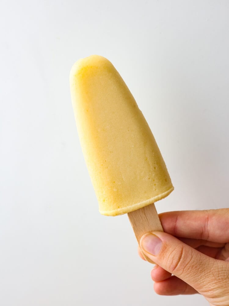 These fresh and fruity homemade popsicles will keep you cool all summer! They're naturally sweetened with honey and coconut milk for a refreshing, tasty treat. Closeup of a yellow popsicle.