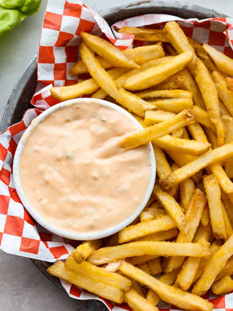 The famous In-N-Out spread is the best part of the burgers and fries at the popular west coast restaurant. Now you can enjoy this sweet and tangy condiment at home with this copycat recipe for In-N-Out spread. Overhead photo of a French fry dipping in a bowl of sauce. The small bowl of sauce and extra French fries are inside of a metal tin pan. The metal tin pan is lined with red and white checkered parchment paper.