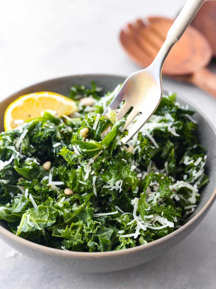 If youโre looking for a tasty way to incorporate more leafy greens into your diet, this is it! This kale salad is tossed with parmesan, lemon, and pine nuts for a bright and fresh flavor combination you won't be able to resist! Closeup of a fork skewering a bite of lemon parmesan kale salad.