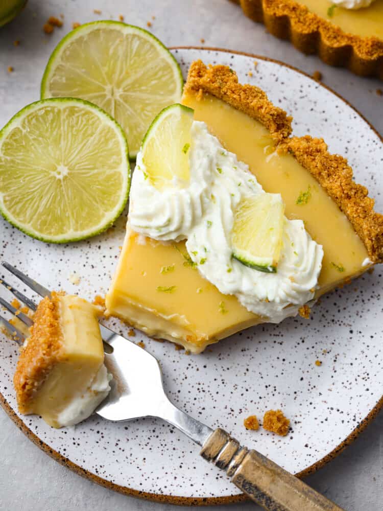 This traditional key lime tart with a graham cracker crust is a must-make dessert for the summer! Each bite is creamy, juicy, and the perfect balance of tart and sweet! Closeup of a tart slice with a bite taken out of it with a fork.