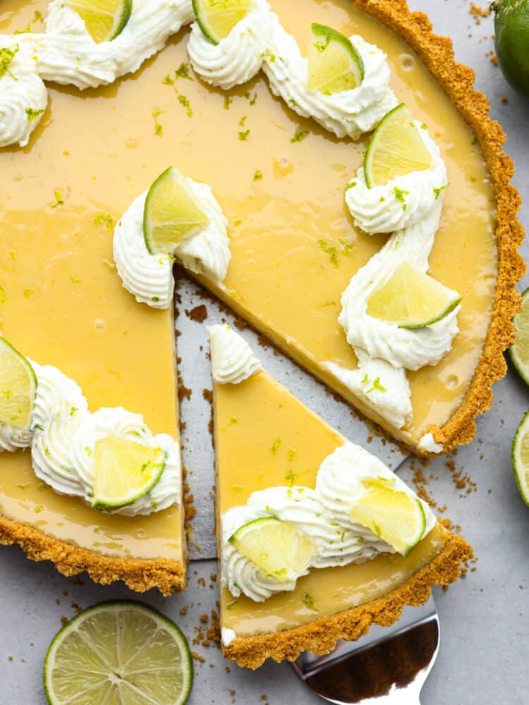 This traditional key lime tart with a graham cracker crust is a must-make dessert for the summer! Each bite is creamy, juicy, and the perfect balance of tart and sweet! Top-down view of a slice of key lime tart being picked up with a pie server.