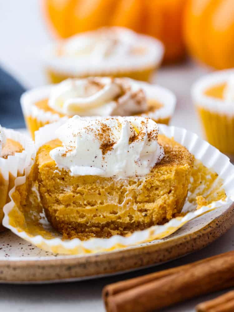 These mini pumpkin cheesecakes are the perfect dessert for any fall gathering! Individual-sized and full of pumpkin flavor, they are everything you love about pumpkin pie and cheesecake all in one. These mini desserts are sure to be your new holiday tradition. Closeup of a mini pumpkin cheesecake, cut so the inside can be seen.