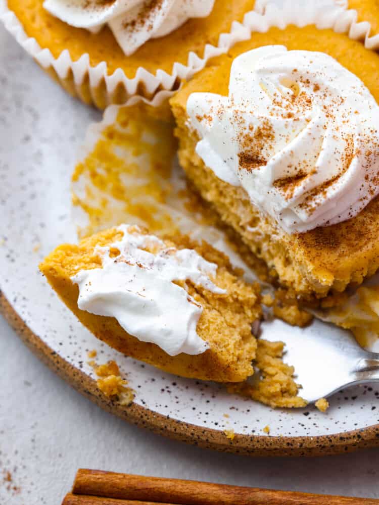 These mini pumpkin cheesecakes are the perfect dessert for any fall gathering! Individual-sized and full of pumpkin flavor, they are everything you love about pumpkin pie and cheesecake all in one. These mini desserts are sure to be your new holiday tradition. Closeup of cheesecake topped with whipped cream and dusted with cinnamon. There is a piece cut out by a metal fork.