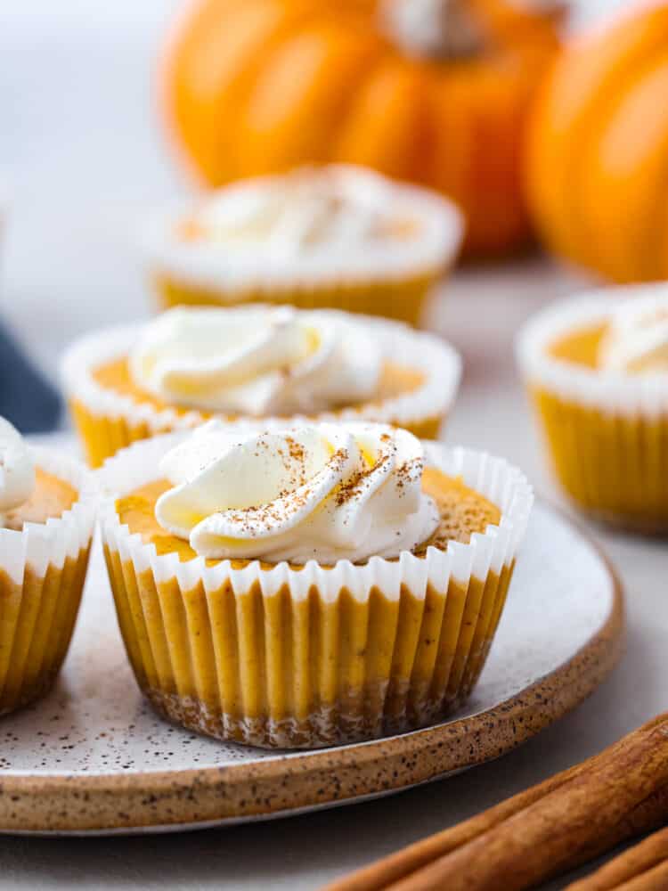 These mini pumpkin cheesecakes are the perfect dessert for any fall gathering! Individual-sized and full of pumpkin flavor, they are everything you love about pumpkin pie and cheesecake all in one. These mini desserts are sure to be your new holiday tradition. Closeup of a mini pumpkin cheesecake served on a stoneware plate.