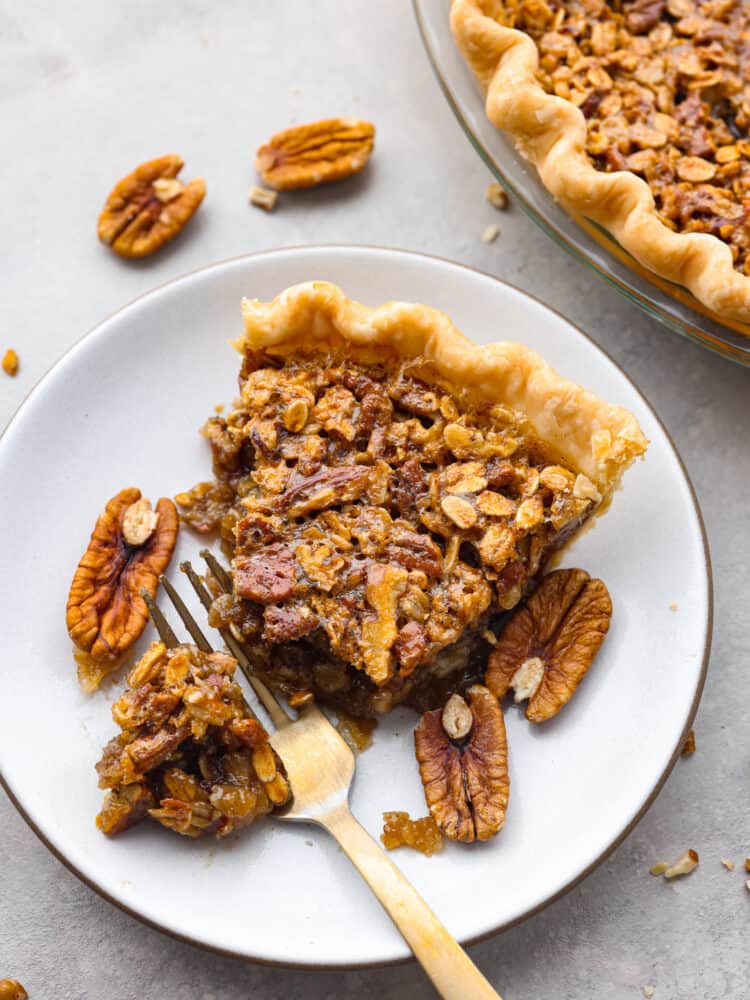 If you love pies, then this delicious and unique oatmeal pecan pie is for you! And if you haven't made a pie before, do not fear... this recipe really is so easy! A slice of oatmeal pecan pie on a plate with a gold fork cutting out a piece to eat.