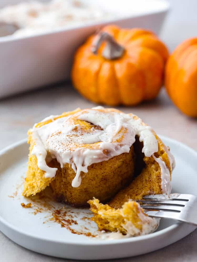 Pumpkin cinnamon rolls are filled with a delicious brown sugar filling and smothered in homemade cream cheese frosting. Soft, fluffy and so perfect for fall! Closeup of a pumpkin cinnamon roll served on a white plate.