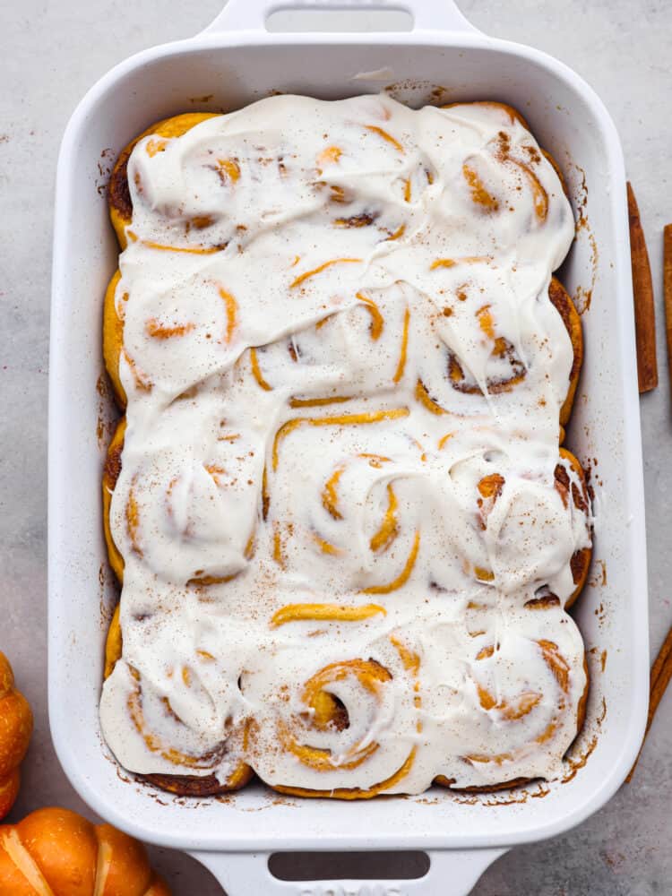 Pumpkin cinnamon rolls are filled with a delicious brown sugar filling and smothered in homemade cream cheese frosting. Soft, fluffy and so perfect for fall! Top-down view of an entire pan of pumpkin cinnamon rolls.
