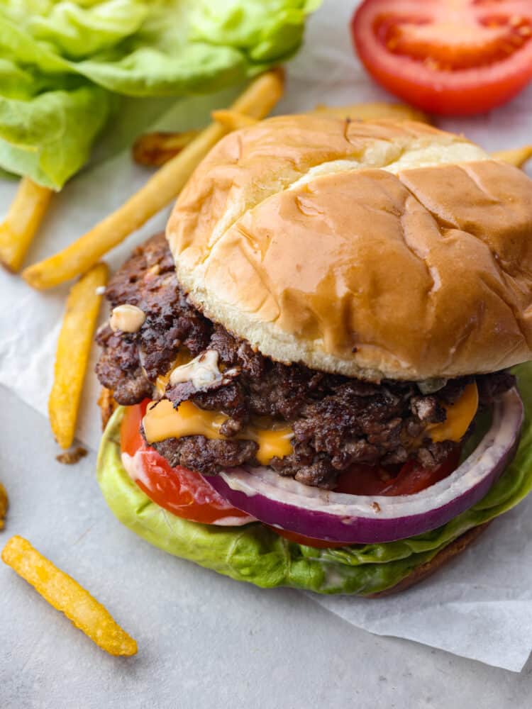 I love a good burger! Smash burgers are easy to prepare and come together so fast. If ever I'm craving a good old-fashioned burger, these smash burgers are my go-to recipe! Top view of smash burger with top bun slightly off centered so you can see the meat, onion, lettuce, and cheese. Fries on the side.