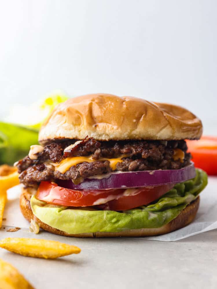 I love a good burger! Smash burgers are easy to prepare and come together so fast. If ever I'm craving a good old-fashioned burger, these smash burgers are my go-to recipe! Close up side view of smash burger in a soft toasted bun, and ayered with meat, cheese, red onion, tomato and lettuce.