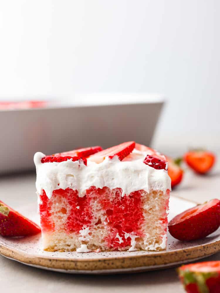 Incredibly light and tasty, this strawberry poke cake will be the star of any gathering! It's airy, soft, and brings that fresh strawberry taste into every single bite! The side view of a slice of poke cake on a plate.