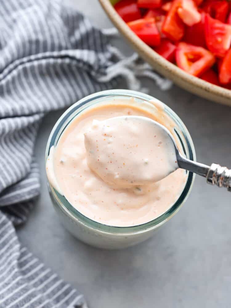 Sweet and tangy all at the same time, this thousand island dressing is just what every salad needs! It's creamy and packed with delicious flavor. You will want to put it on everything! The top view of thousand isaland dressing and a spoon being dipped into it.