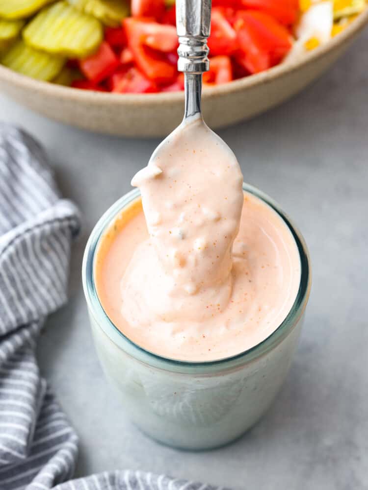 Sweet and tangy all at the same time, this thousand island dressing is just what every salad needs! It's creamy and packed with delicious flavor. You will want to put it on everything! Thousand island dressing in a jar with a spoon being pulled out of it.