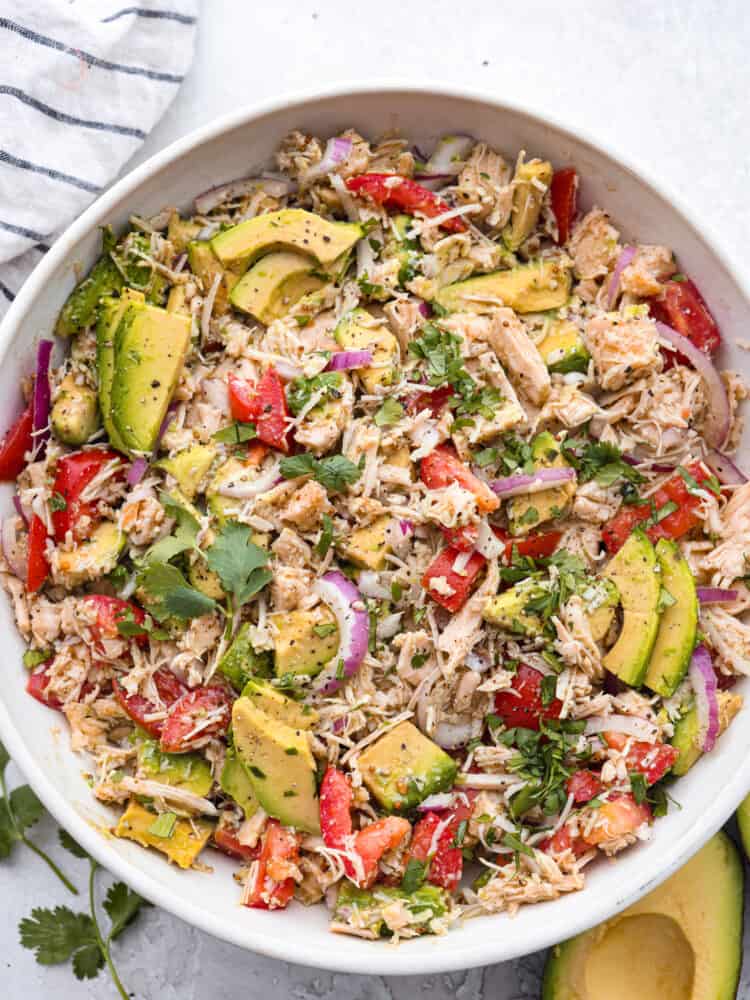 This fresh and flavorful avocado tuna salad is the perfect side dish for summer! The combo of bright veggies, savory tuna, and creamy avocado is one you don't want to miss! Top-down view of tuna salad in a white bowl.