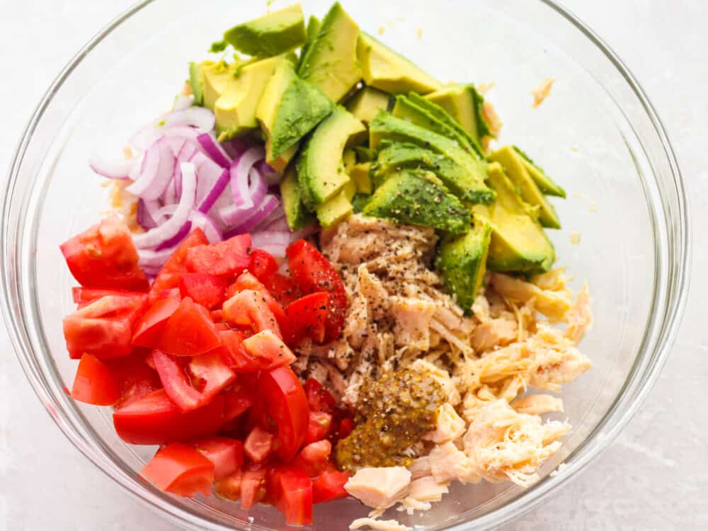 This fresh and flavorful avocado tuna salad is the perfect side dish for summer! The combo of bright veggies, savory tuna, and creamy avocado is one you don't want to miss! Ingredients for avocado tuna salad in a clear bowl, ready to be mixed.