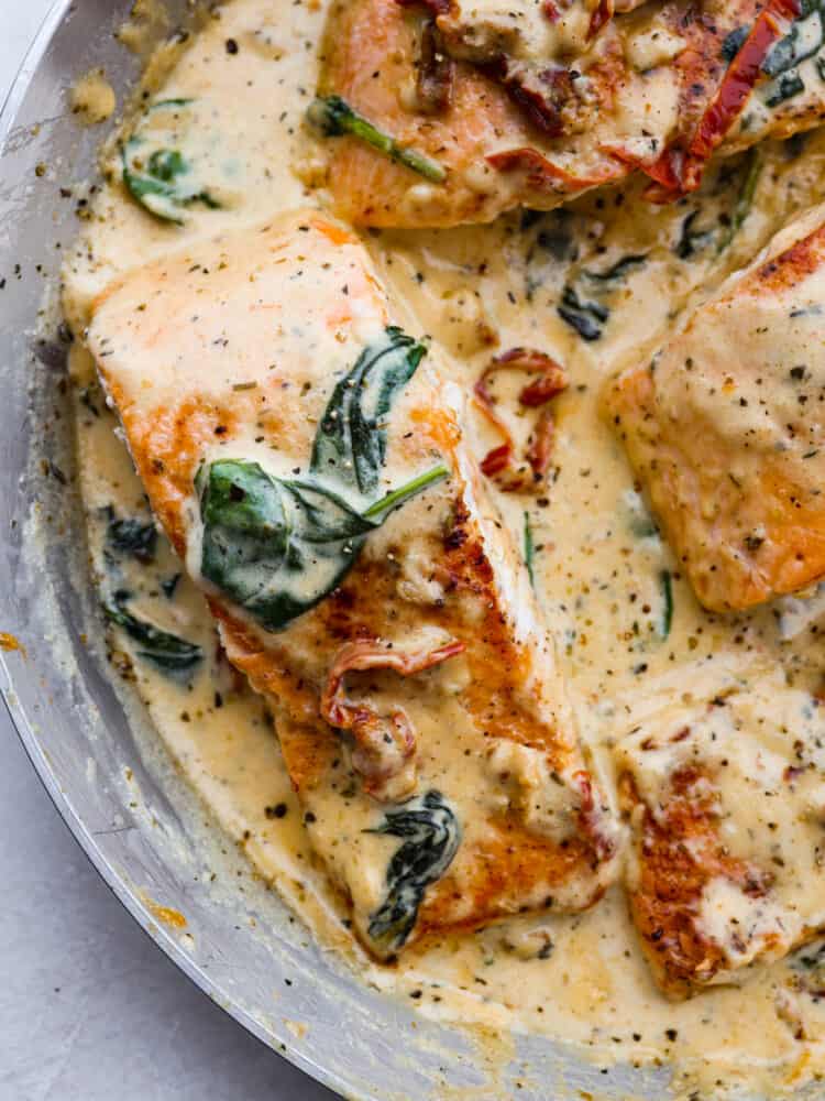 Creamy Tuscan Garlic Salmon is an easy 30 minute restaurant quality meal. The pan seared salmon gets smothered in the most amazing creamy tuscan garlic sauce with sun dried tomatoes and spinach. This is one unforgettable meal! A closeup of creamy tuscan garlic salmon.
