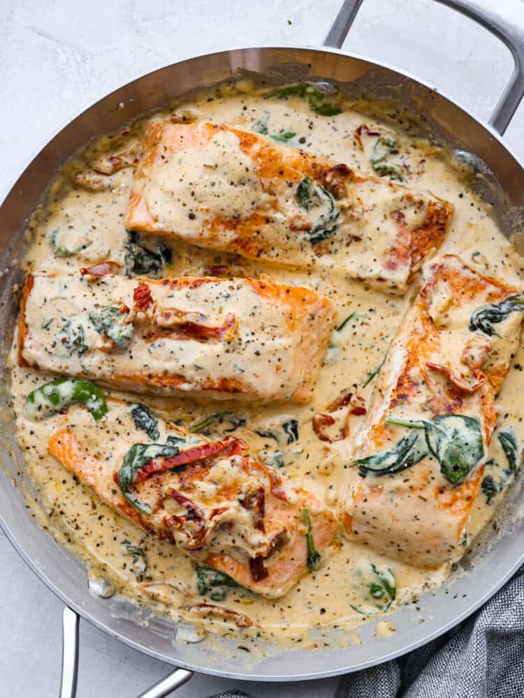 Creamy Tuscan garlic salmon is an easy 30-minute restaurant-quality meal. The pan-seared salmon gets smothered in the most amazing creamy Tuscan garlic sauce with sun-dried tomatoes and spinach. This is one unforgettable meal! A pan with creamy tuscan garlic salmon all cooked.