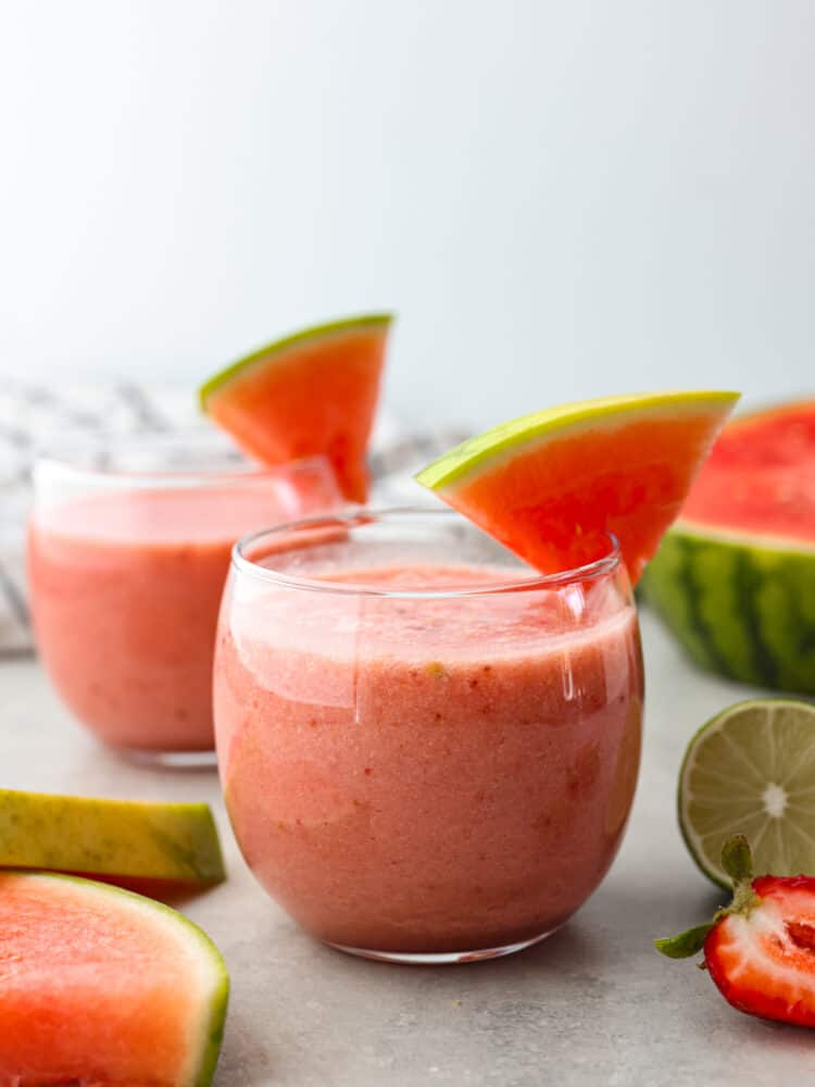 Find out what summer tastes like by drinking a sip of this watermelon smoothie! It's juicy, sweet, and made from the most delicious and flavorful fruit of the season... watermelon! A glass cup filled with watermelon smoothie and a watermelon slice on the side of the cup.