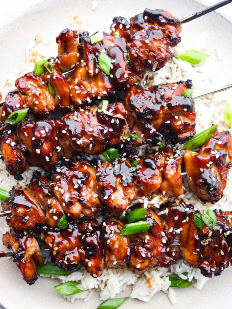 Yakitori chicken skewers are juicy and perfectly charred, topped with a sweet and smoky glaze. Inspired by Japanese street food, they'll be the best thing you grill this summer! Closeup of yakitori skewers on a bed of white rice.