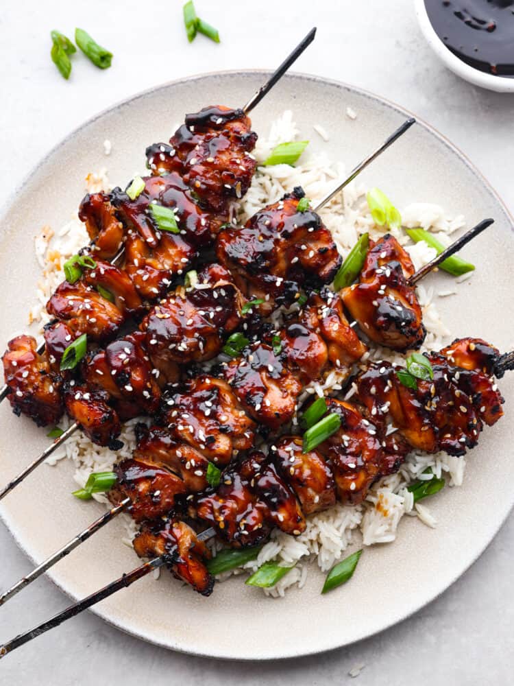 Yakitori chicken skewers are juicy and perfectly charred, topped with a sweet and smoky glaze. Inspired by Japanese street food, they'll be the best thing you grill this summer! Top-down view of chicken skewers on a white plate.
