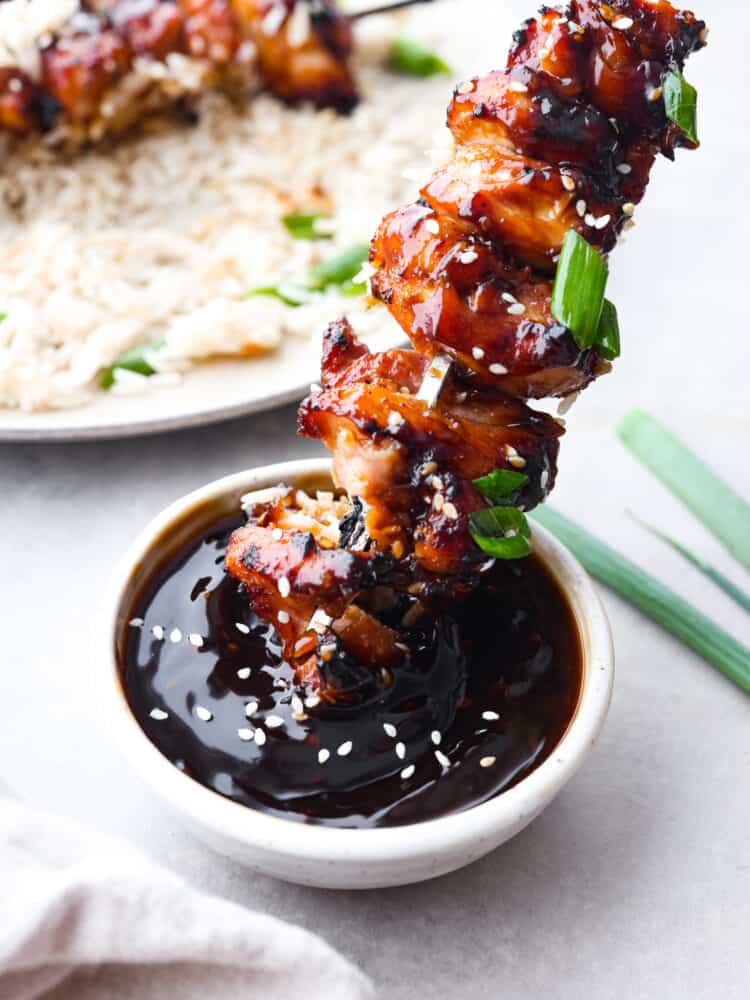 Yakitori chicken skewers are juicy and perfectly charred, topped with a sweet and smoky glaze. Inspired by Japanese street food, they'll be the best thing you grill this summer! Dipping a skewer into yakitori sauce.