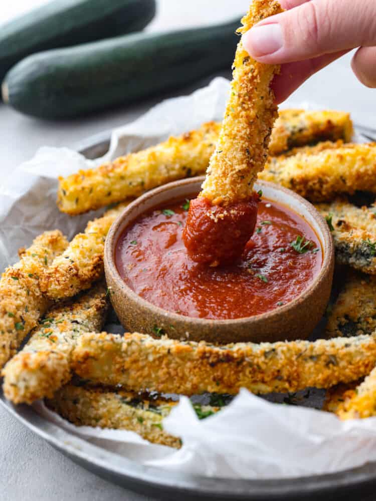 Baked zucchini fries are crispy on the outside with a crunchy, seasoned crust and tender zucchini inside. It's hard to stop after just one! Dipping a fry in marinara sauce.