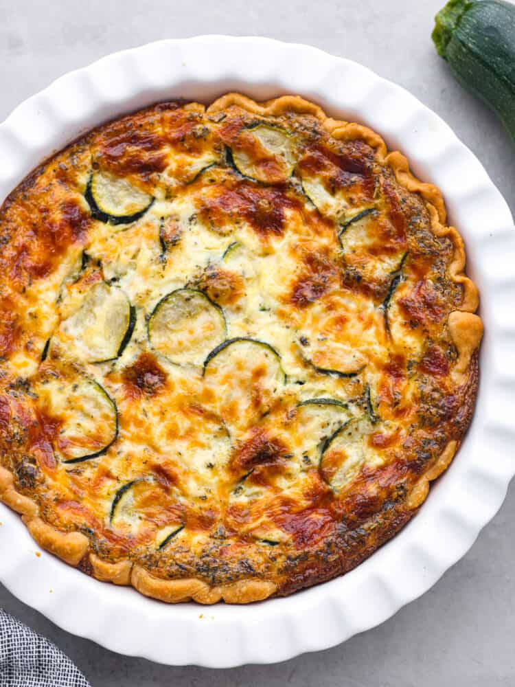 This delicious zucchini quiche has a creamy savory egg mixture baked in a perfectly flaky crust. Layers of melted cheese and zucchini make the texture of this quiche cheesy and flavorful. The top view of a baked zucchini quiche.