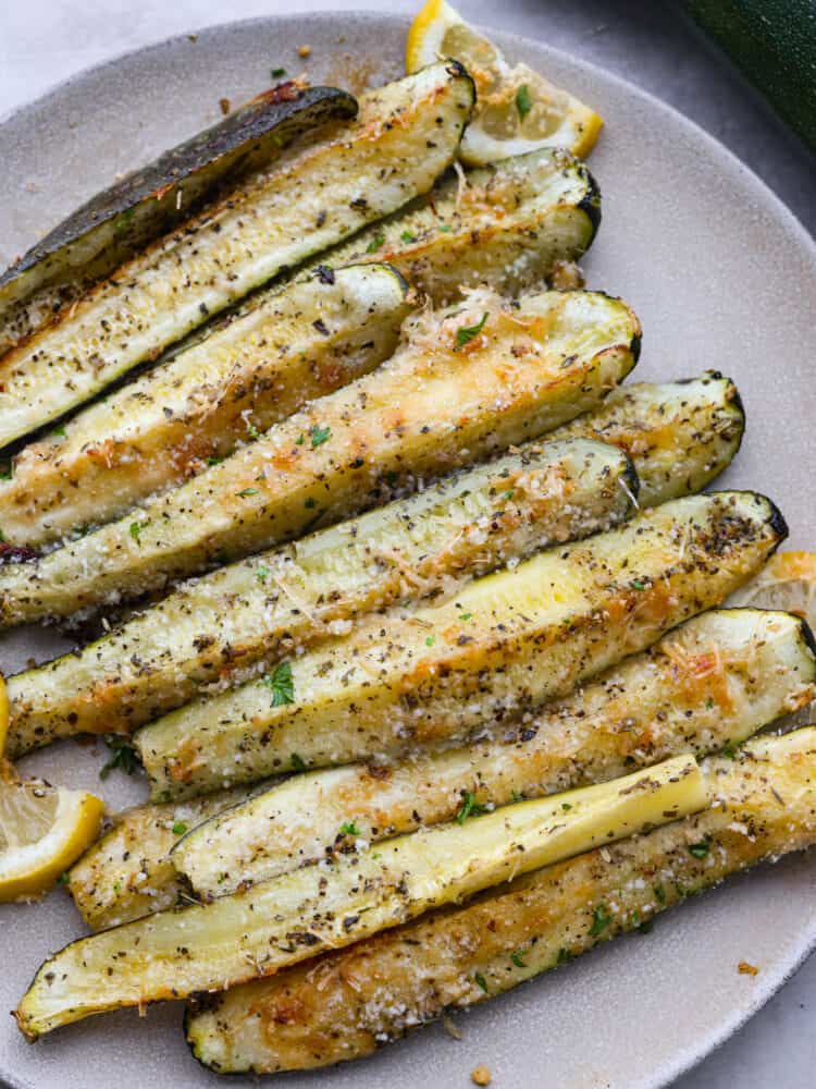 If you're looking for the best way to use up all that summer zucchini, this is it! Quick and easy zucchini spears coated in parmesan and garlic and roasted in the oven to perfection. Top-down view of zucchini spears on a gray plate.