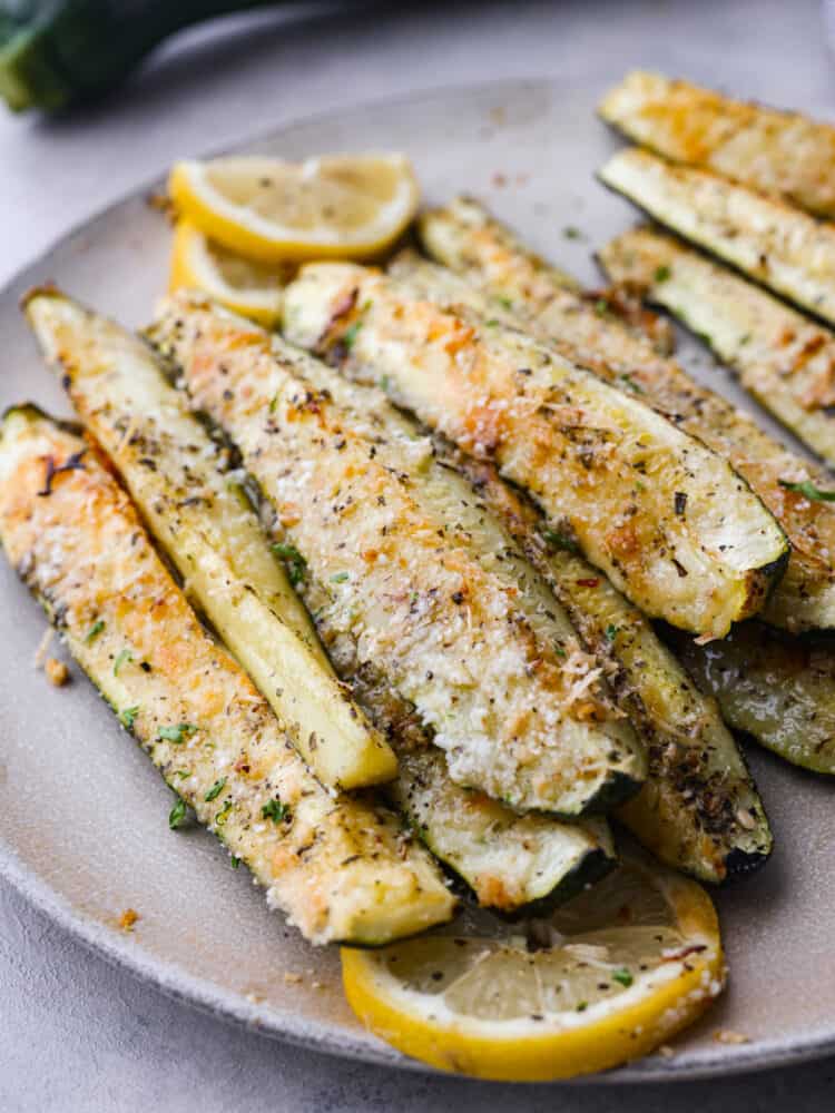 If you're looking for the best way to use up all that summer zucchini, this is it! Quick and easy zucchini spears coated in parmesan and garlic and roasted in the oven to perfection. Roasted parmesan garlic zucchini spears on a gray stoneware plate.