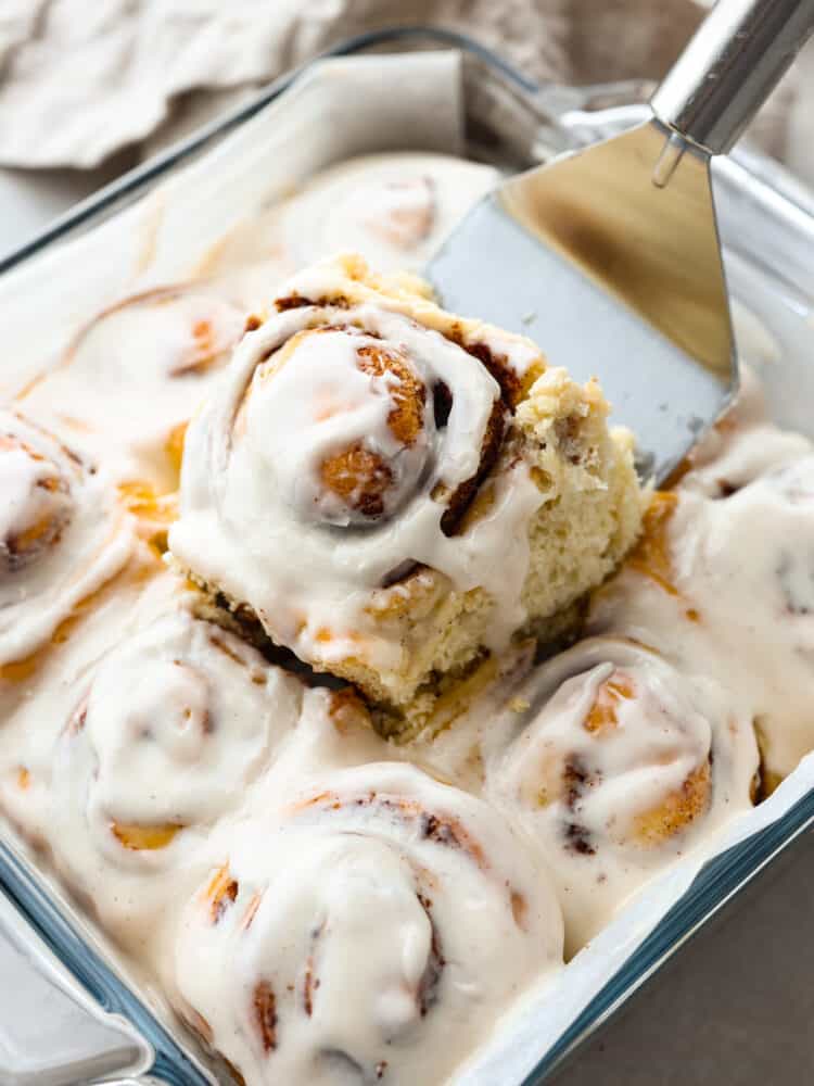 Quick 45 Minute Cinnamon Rolls are made with homemade dough filled with groundย cinnamon, and a brown sugarย mixture rolled and baked in less than an hour. Drizzle a sweet glaze over the top, making this the VERY BEST breakfast! Baked cinnamon rolls in a 9x12 glass baking dish with one being served.