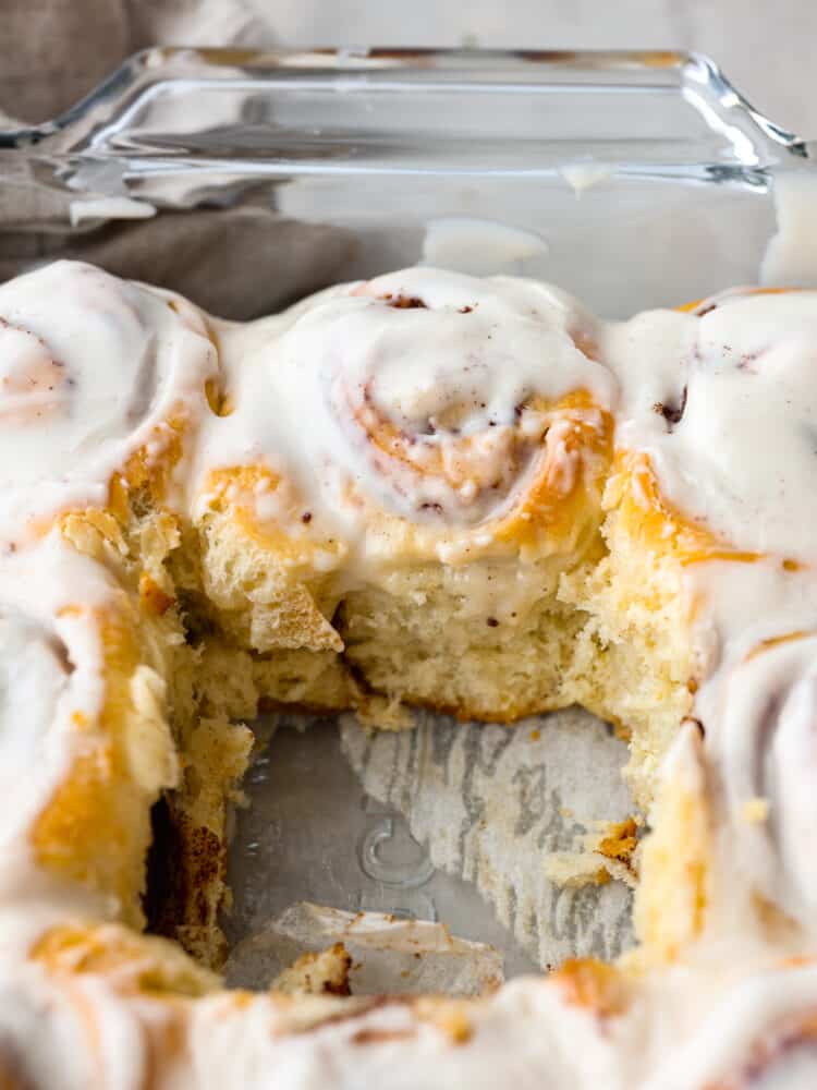 Quick 45 Minute Cinnamon Rolls are made with homemade dough filled with groundย cinnamon, and a brown sugarย mixture rolled and baked in less than an hour. Drizzle a sweet glaze over the top, making this the VERY BEST breakfast! A pan with cinnamon rolls with one roll that is taken out.