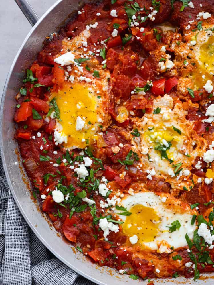 Shakshuka is an amazing one-pan meal consisting of poached eggs in a savory tomato sauce seasoned with flavorful herbs and spices! It's so simple but incredibly delicious! You'll love the bold and bright flavors inspired by North African cuisine. Closeup of shakshuka in a metal skillet.
