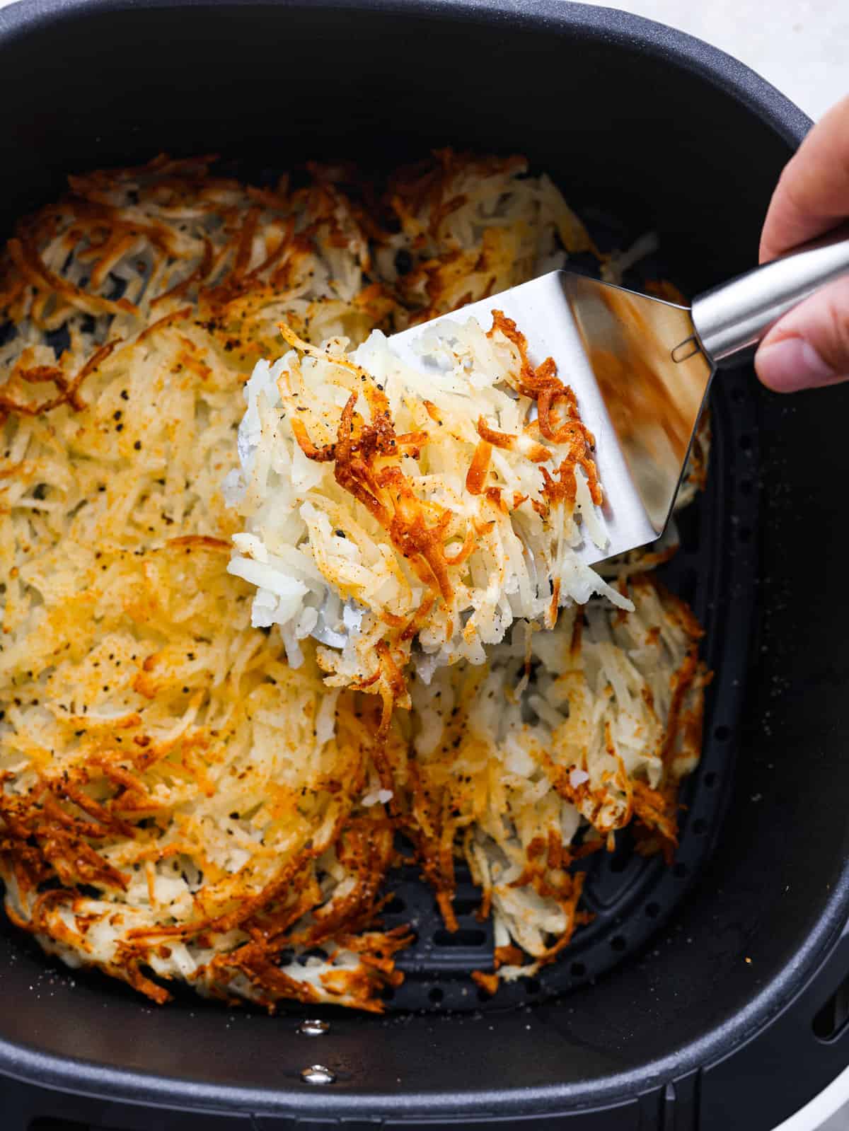 My air fryer is one of my favorite appliances in the kitchen because it can cook all my familyโs favorite recipes, including tender meats, roasted sides, crispy appetizers, and everything in between. A picture of hash browns being served out of a pan.