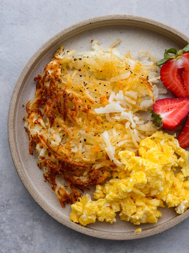 Make mornings easier with these air fryer hash browns cooked perfectly in minutes! Crispy, golden, and seasoned to taste like your favorite diner hash browns. Top view photo of hash browns on a tan colored plate. Sliced whole strawberries garnished on the side.