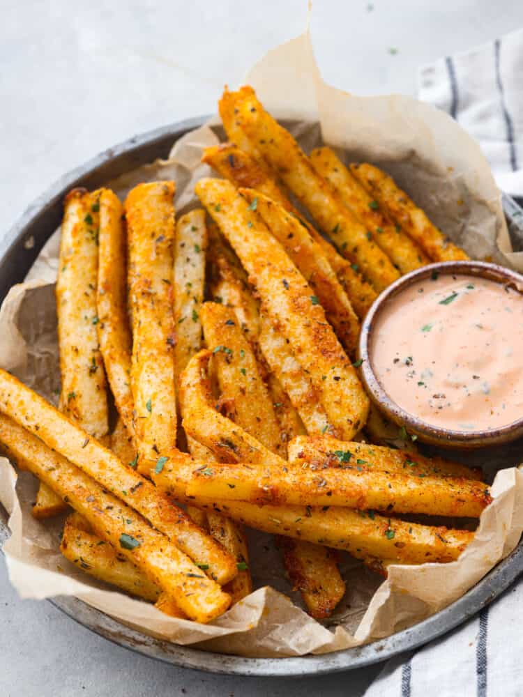 These delicious baked jicama fries are a low-carb alternative to French fries and are coated with savory seasonings! They're oven-roasted for that perfect crispy, golden brown outer layer. Closeup of jicama fries, served with dipping sauce in a gray bowl.