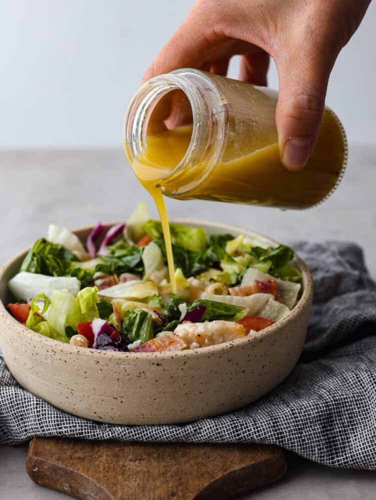 Apple cider vinaigrette is a staple dressing for adding a burst of bright, tangy flavor to your favorite salads. Make it from scratch and you won’t want it any other way! Apple cider vinaigrette being poured over a salad.