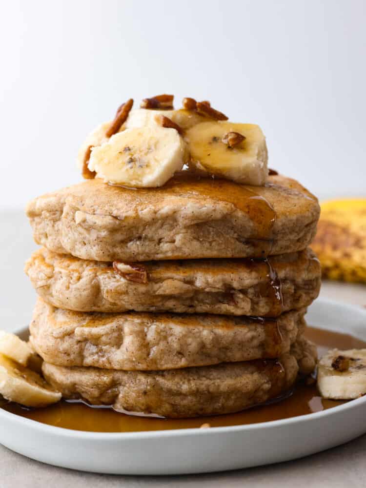 These banana pancakes are perfectly soft and fluffy and taste just like warm banana bread... in pancake form, of course! It's a great recipe to use when you have any over-ripe bananas! A stack of banana pancakes on a plate topped with fresh bananas and pecans.