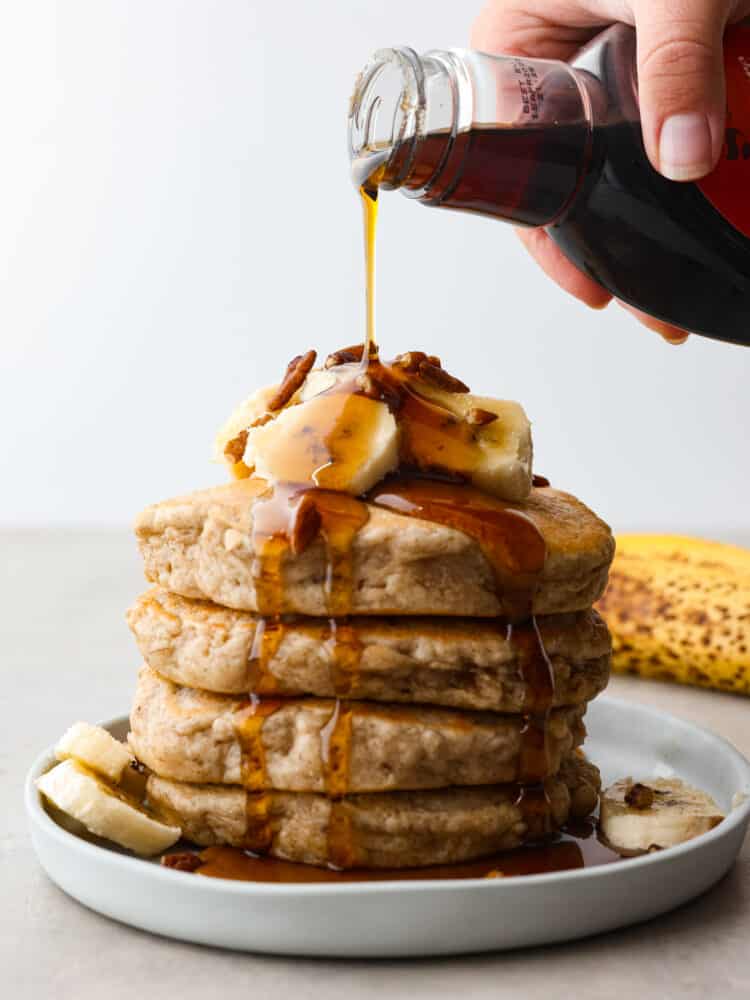 These banana pancakes are perfectly soft and fluffy and taste just like warm banana bread... in pancake form, of course! It's a great recipe to use when you have any over-ripe bananas! A stack of banana pancakes with a homemade vanilla maple glaze being poured on top.