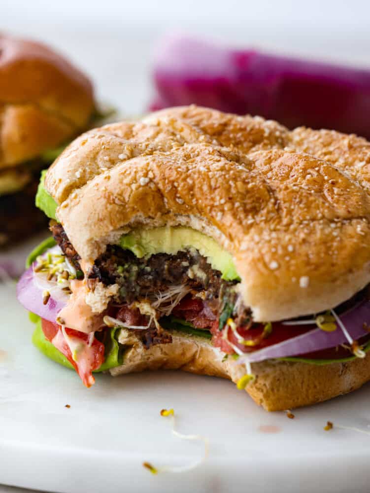 The tender meat-like texture of this black bean burger is packed with incredible flavor. Black beans blended in a mixture of veggies, flavorful herbs, and panko breadcrumbs create an amazing black bean burger that will impress everyone. A close-up photo of an assembled black bean burger with a bite out of it.