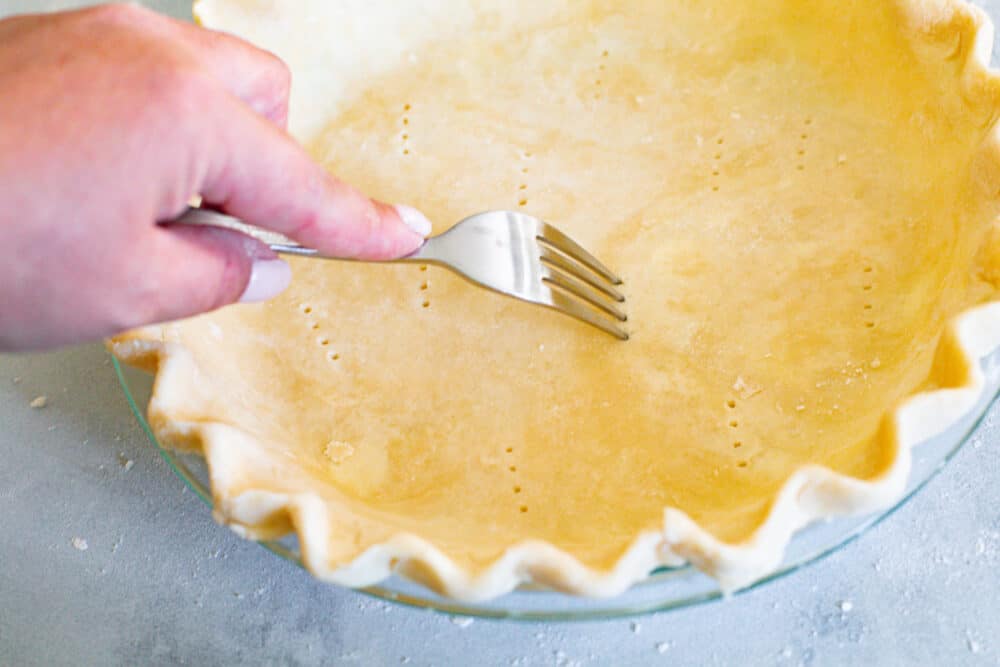 Blind baking a pie crust is key to the perfect pie. I'm going to show you how to do it and why it's so important! Pricking holes in the bottom of a pie crust using a fork.