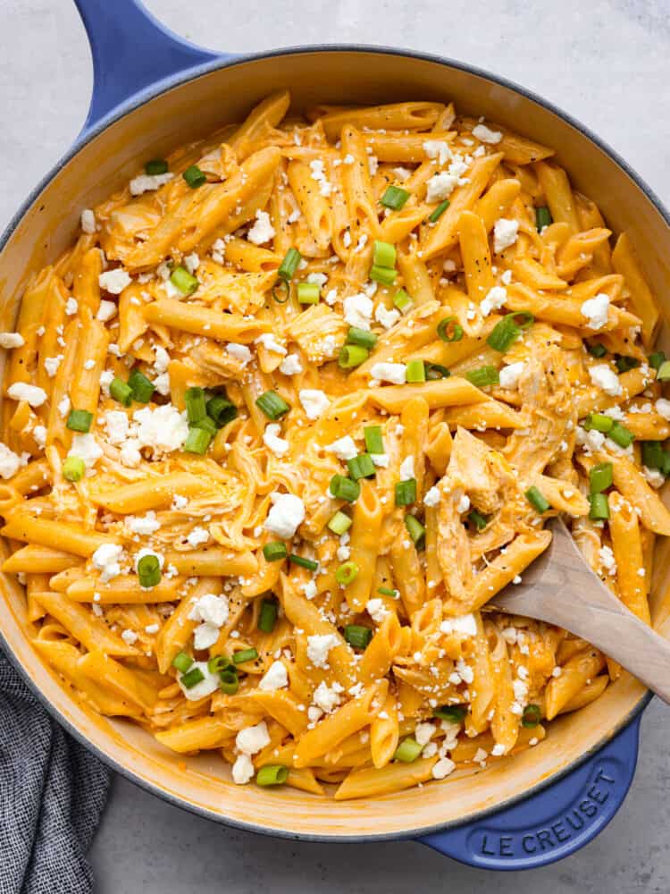 Get that classic buffalo flavor and combine it with some chicken and pasta, and you have yourself a mouthwatering entree that everyone will go crazy over! A skillet with cooked buffalo chicken pasta and a wooden spoon.