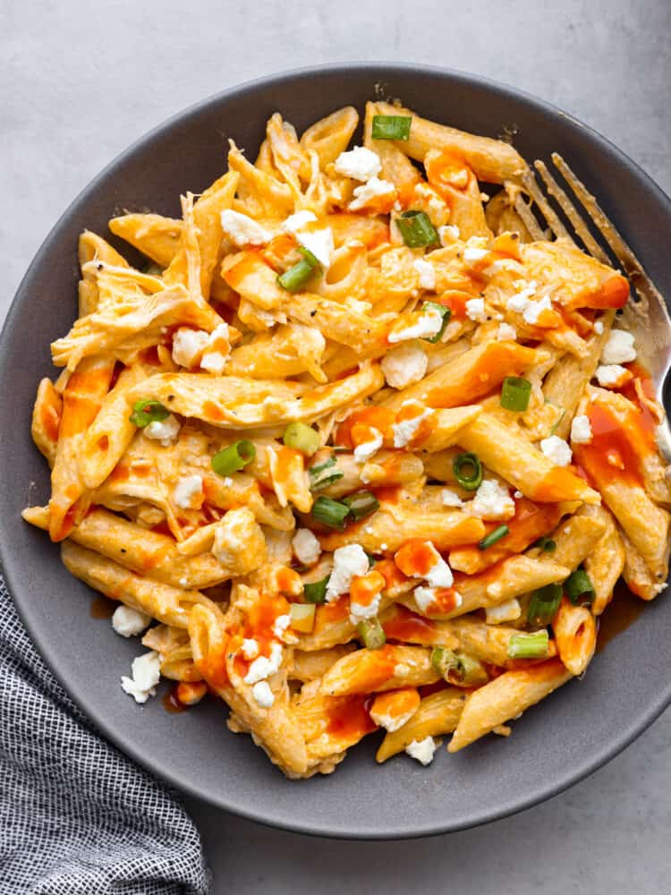 Get that classic buffalo flavor and combine it with some chicken and pasta, and you have yourself a mouthwatering entree that everyone will go crazy over! A gray bowl filled with buffalo chicken pasta garnished with blue cheese crumbles and green onions.